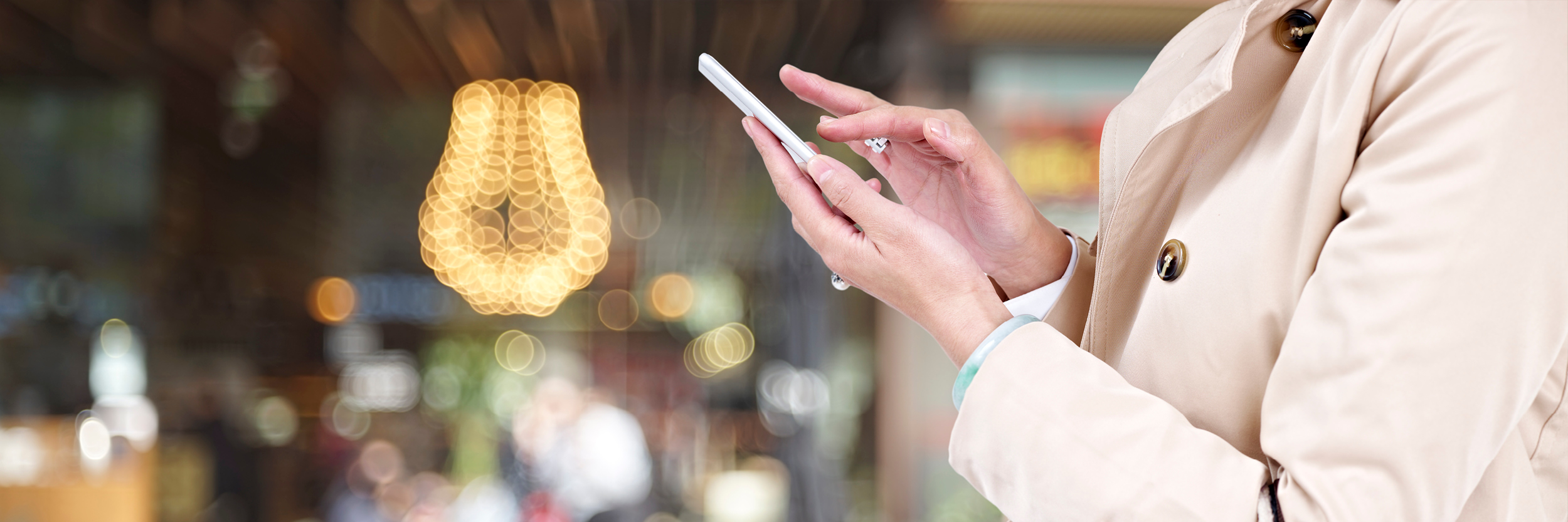 A woman in a raincoat is seen with her phone in her hand.