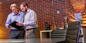 Two men reviewing business documents in a room with brick walls.