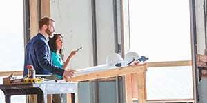 Architect and client on a construction site standing at a drafting table discussing the building process.