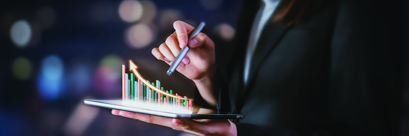 A woman holds an iPad and is pointing at a line chart graphic with a pen