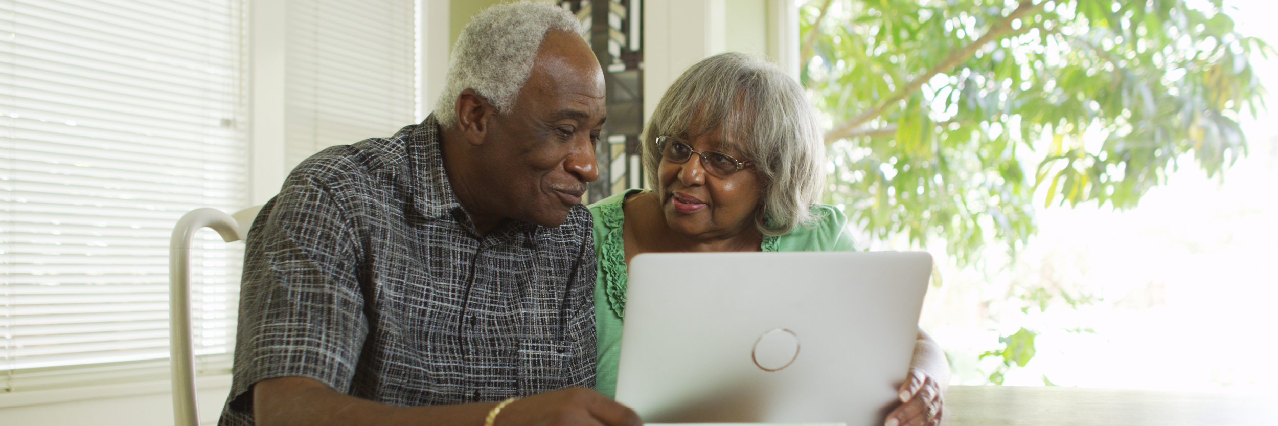 A man and a woman sit at a table, looking at a laptop.