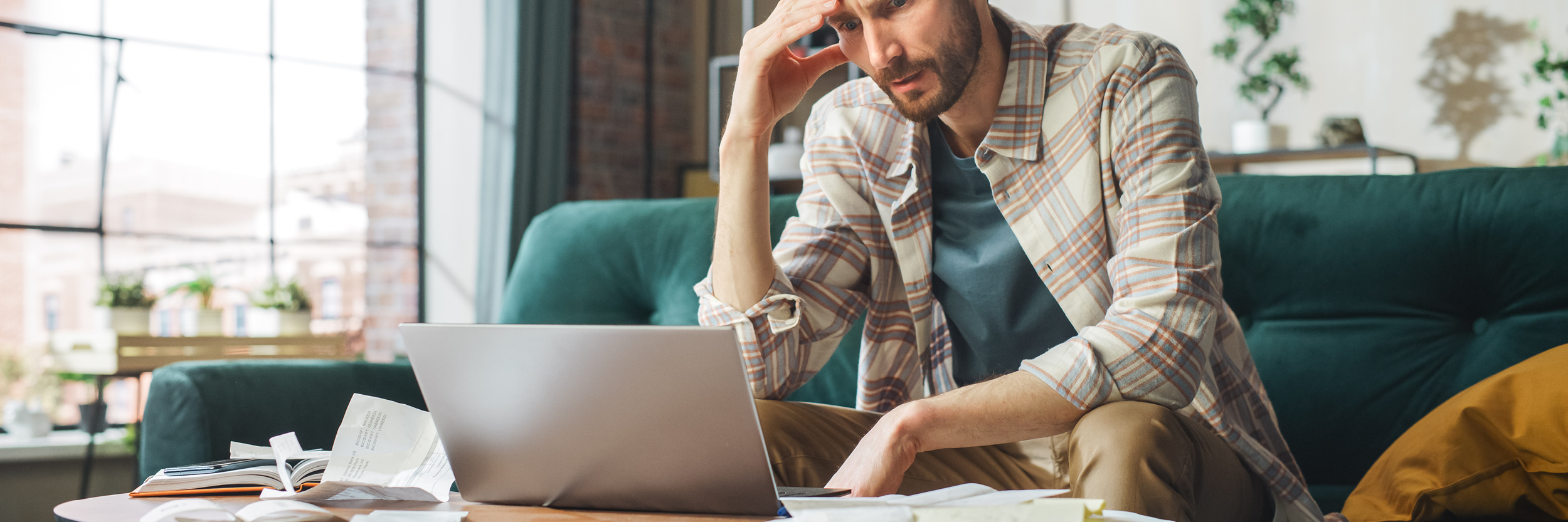 A man sits on a couch looking at his laptop.