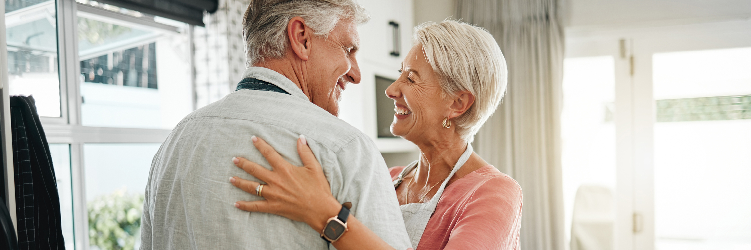 A mature man and woman dance in a kitchen.