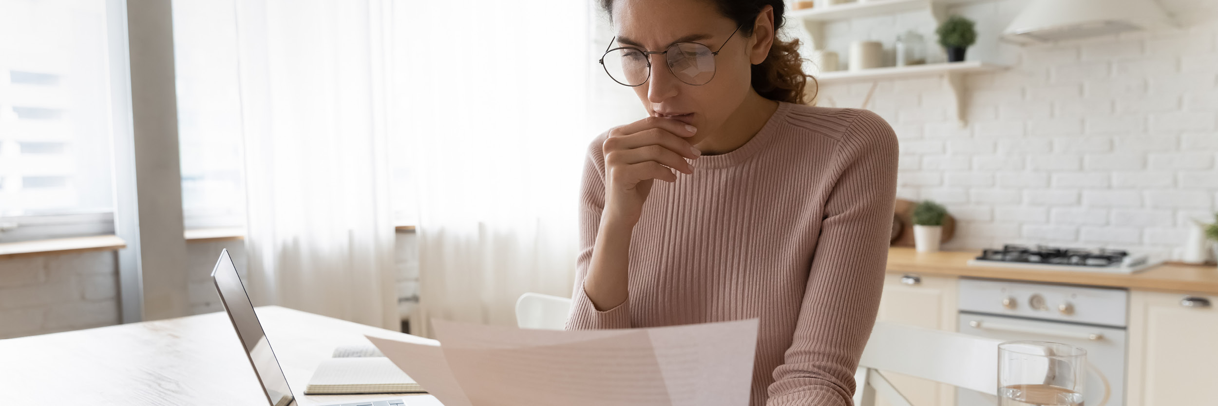 A woman wearing glasses sits at a table looking at some paperwork.