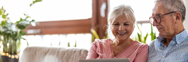 A man and woman sit on a couch looking at a laptop