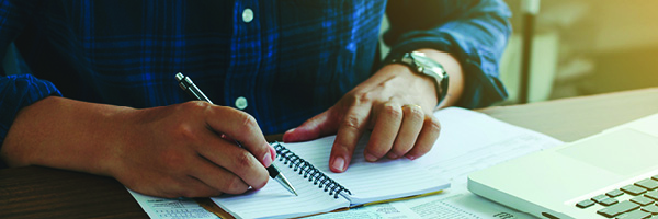 A man's hands are shown as he is writing in a notebook