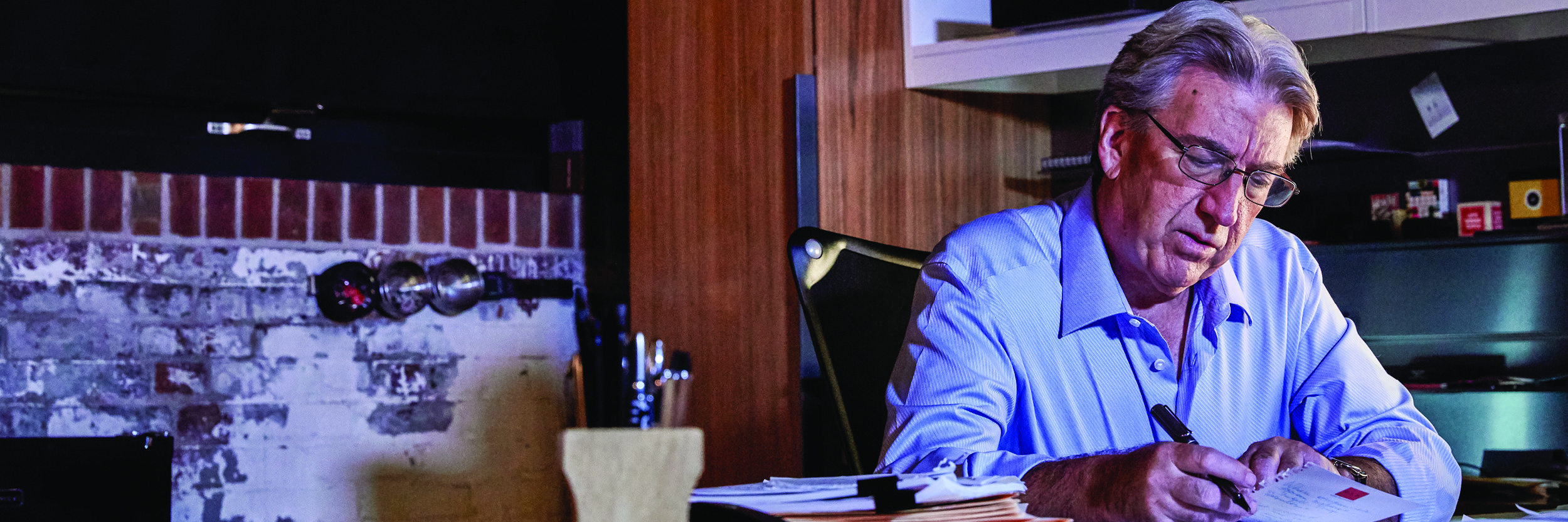 A man sits at a table looking at paperwork with a pen in his hand.