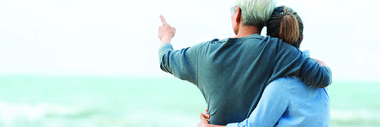 A man and woman look at the ocean and the man points at something unseen