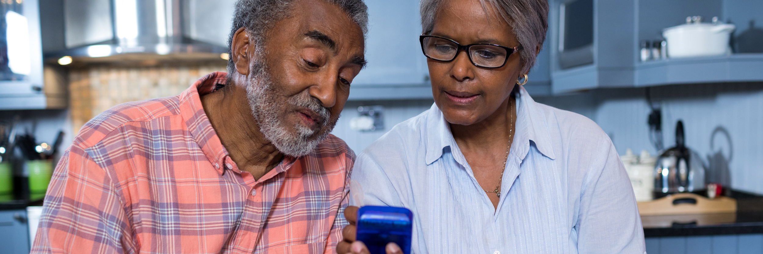 An older man and woman sit at a table, looking at a cell phone.