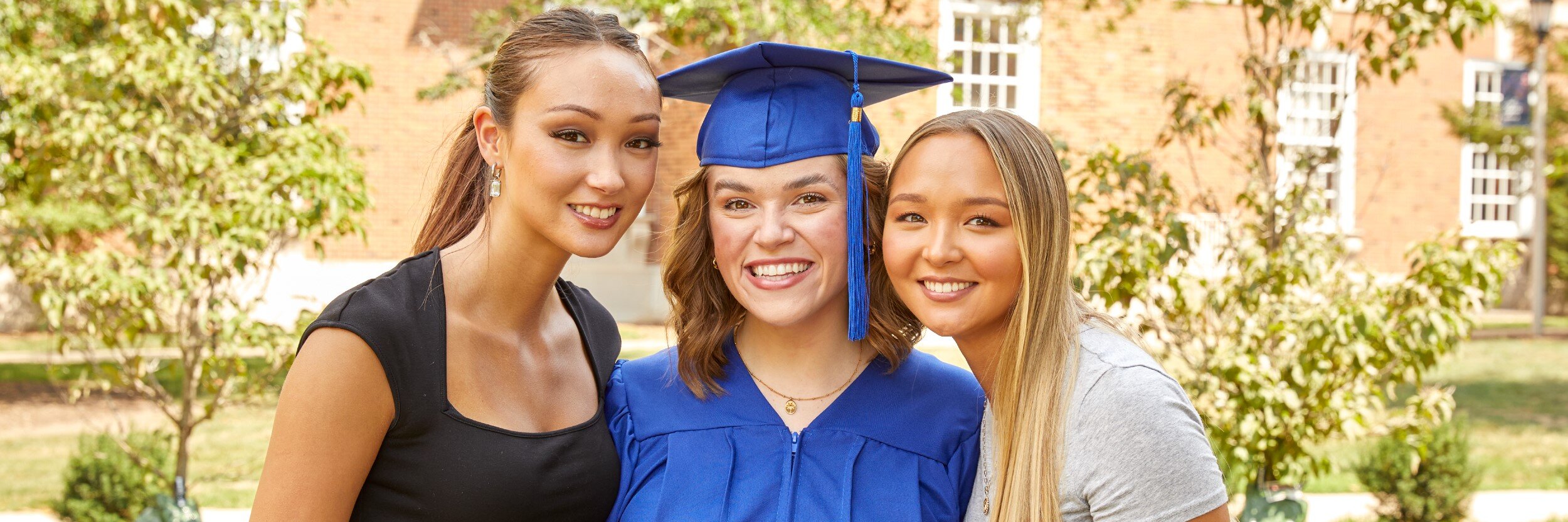 Two women pose with another woman wearing a graduation cap and gown.