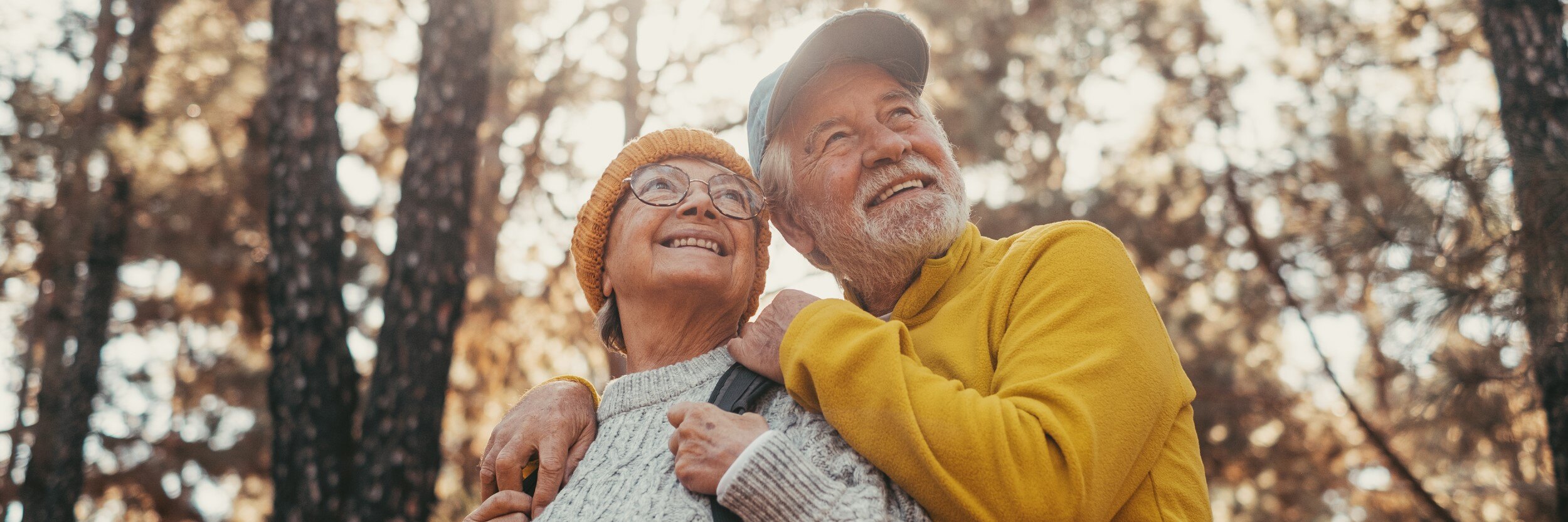 An older man and woman hike in the woods.