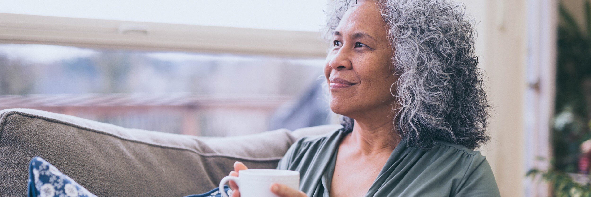  A woman sits on a couch, holding a coffee mug.