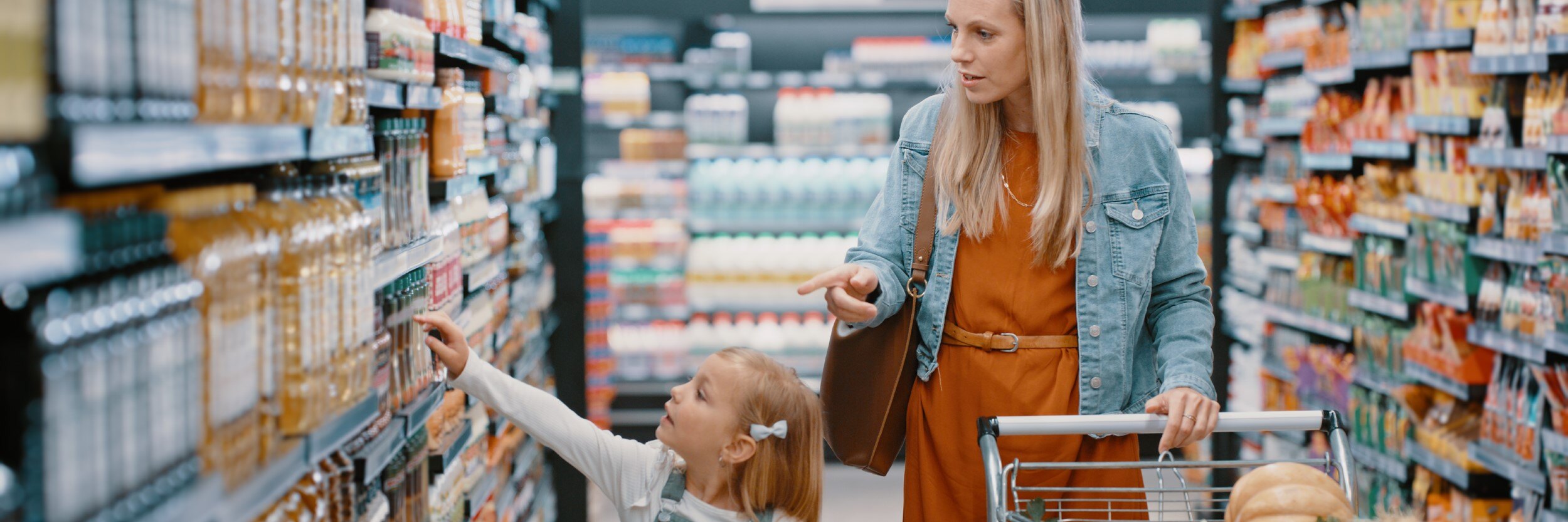 A mom and young daughter are at a grocery store. The mother is pushing a cart.