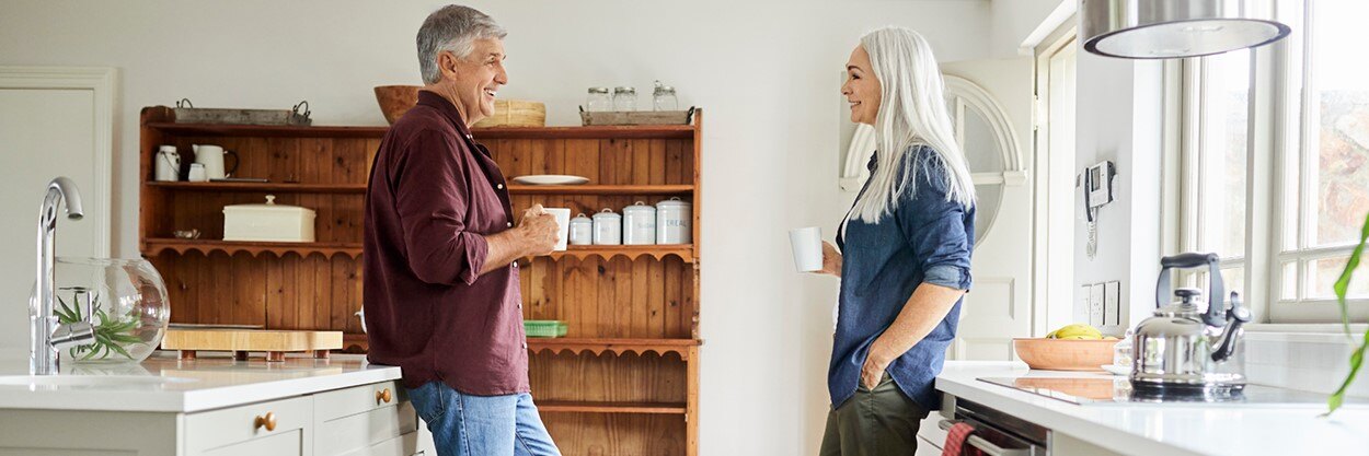 A man and woman standing facing each other in a kitchen, while holding coffee cups.