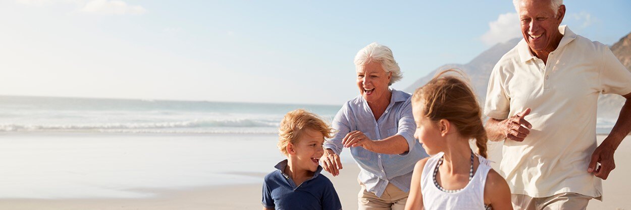 An older man and woman run on a beach with a young girl and boy.