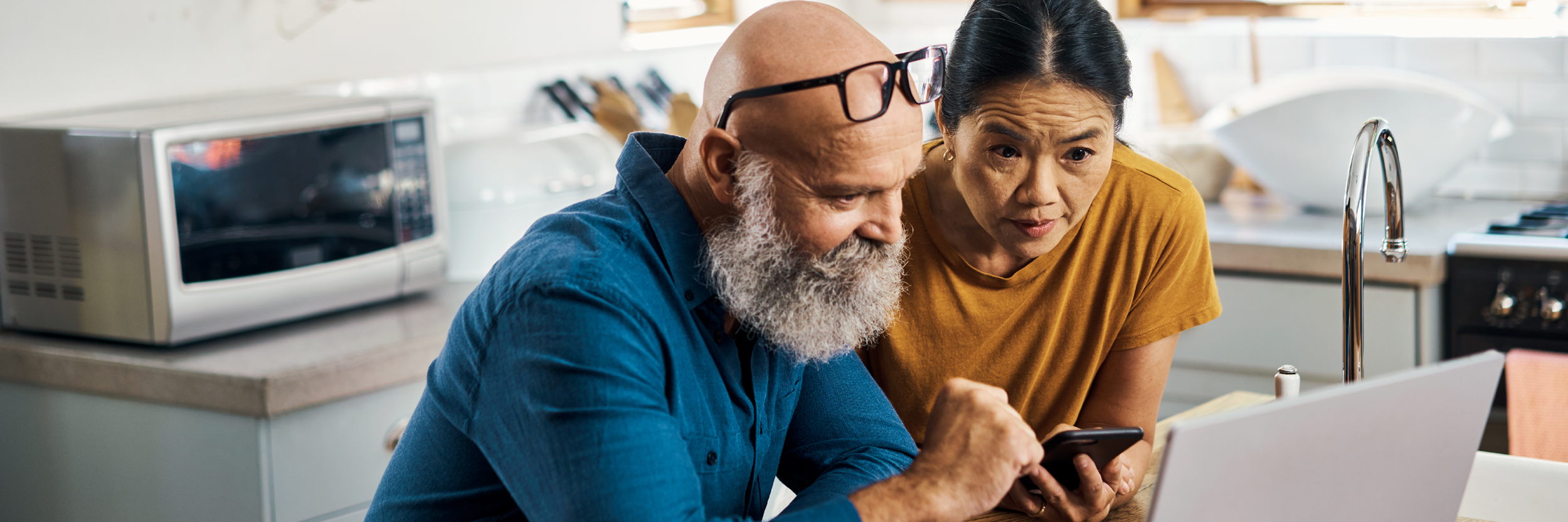 A man and a woman look at a laptop in their kitchen.
