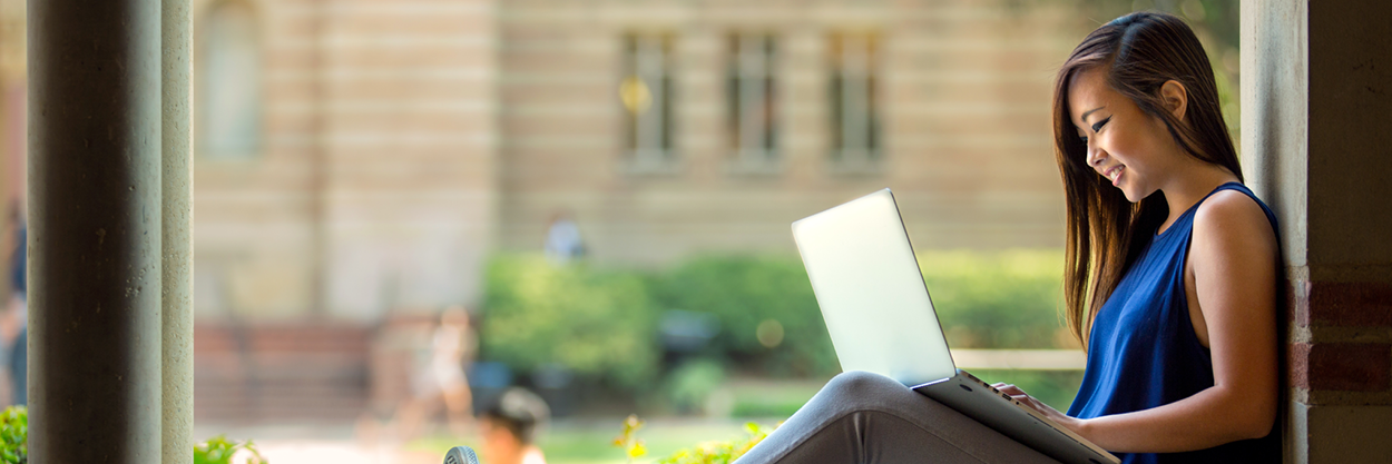 A young woman sits on a wall with a laptop.