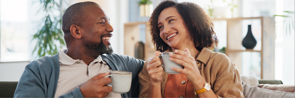 A man and woman sit on a couch, holding coffee cups.