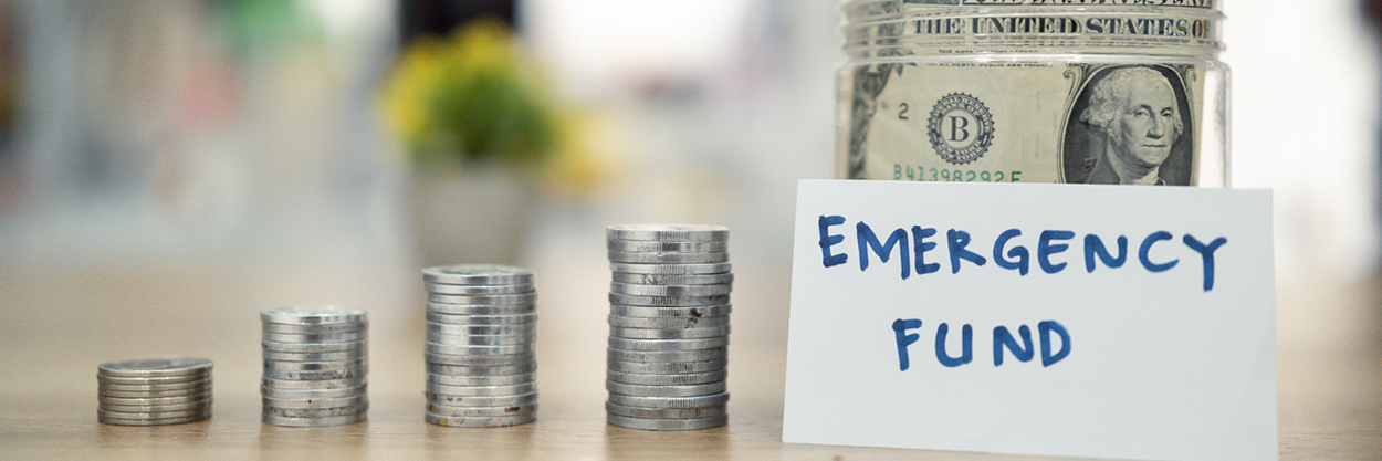 Four stacks of coins, a jar of dollar bills and a sign that reads, Emergency Fund