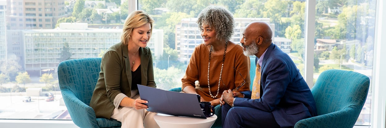 A man and woman are sitting at a table, talking to another woman who has a laptop.