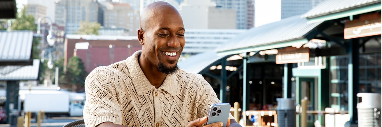 A man sits outside, looking at his cell phone.