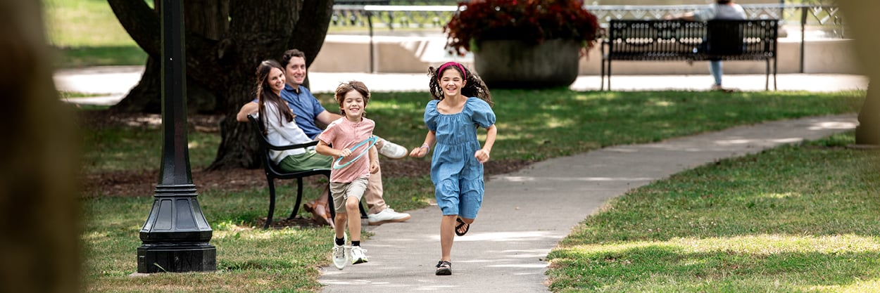 A couple sit on a bench, watching two children running.