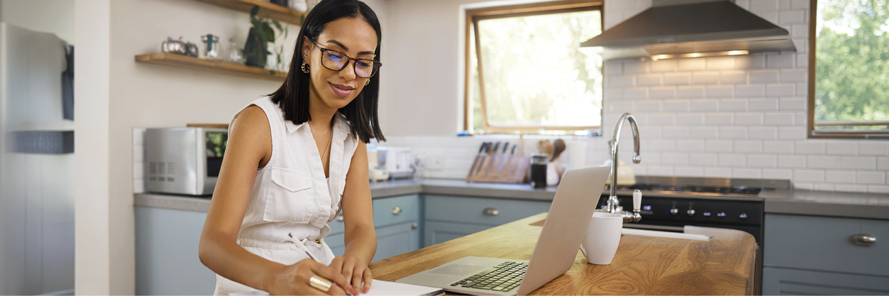 A woman sits in a kitchen with a laptop on the counter.