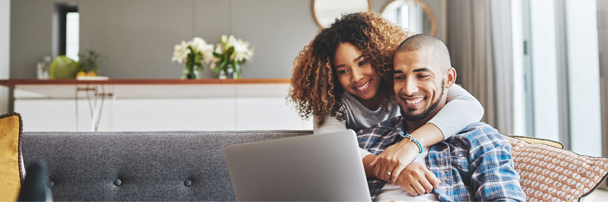 A woman hugs a man as they look at a laptop.