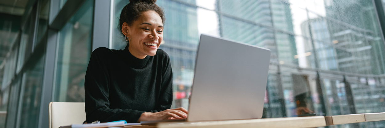 A woman sits at a desk, looking at her laptop