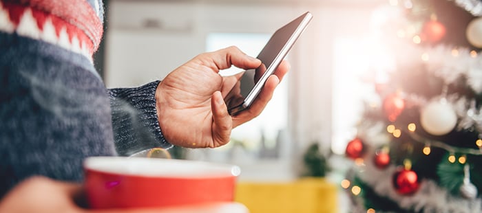 A person stands at a table, holding their cell phone