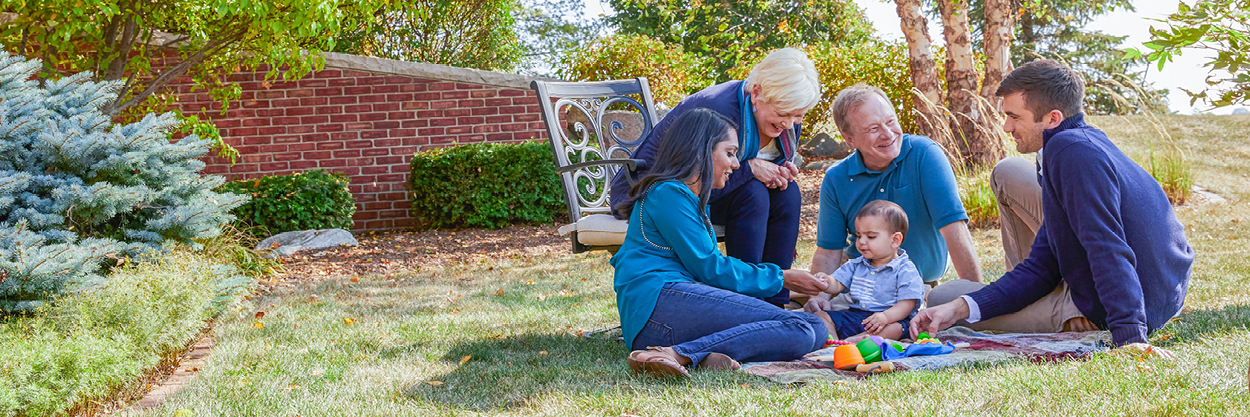 Two women and two men sits on a blanket in the grass with a young boy.