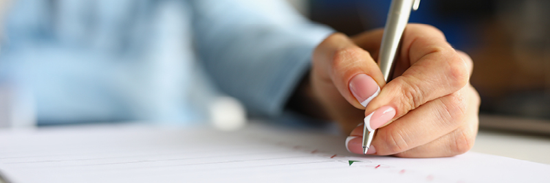 A woman's hand is seen as she holds a pen and writes on a piece of paper.