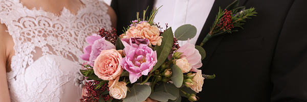 A bridge and groom are partly seen and the bride is holding a bouquet of flowers.