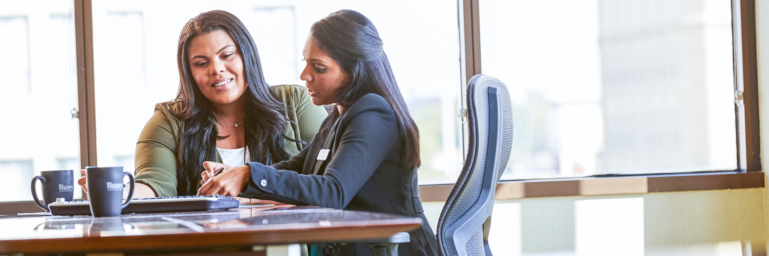 Two women sit at a conference table looking at some documents.