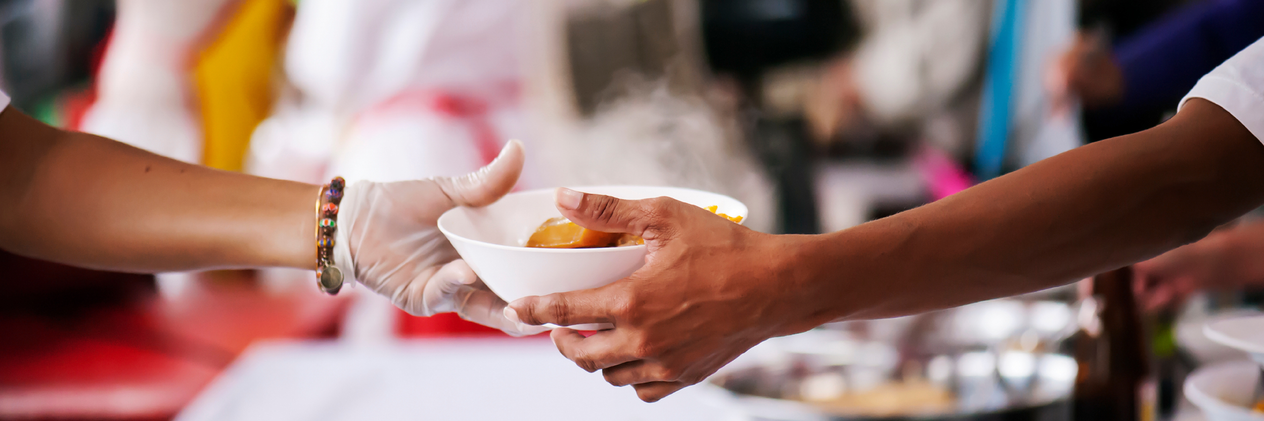 A hand is seen giving a bowl of food to another hand.