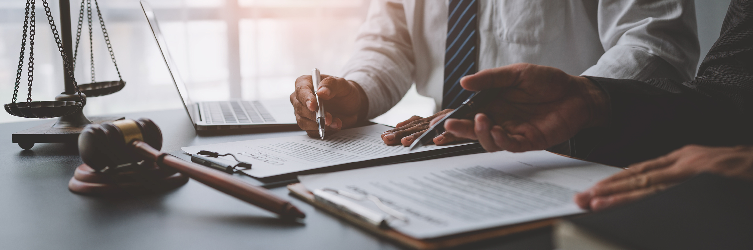 Two men sit at a table looking at paperwork. Only their hands are seen.