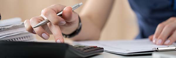 An individual's fingers shown using a calculator, while they're also holding a pen.