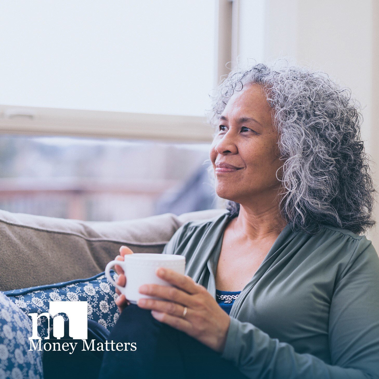 A woman sits on a couch, holding a coffee mug.