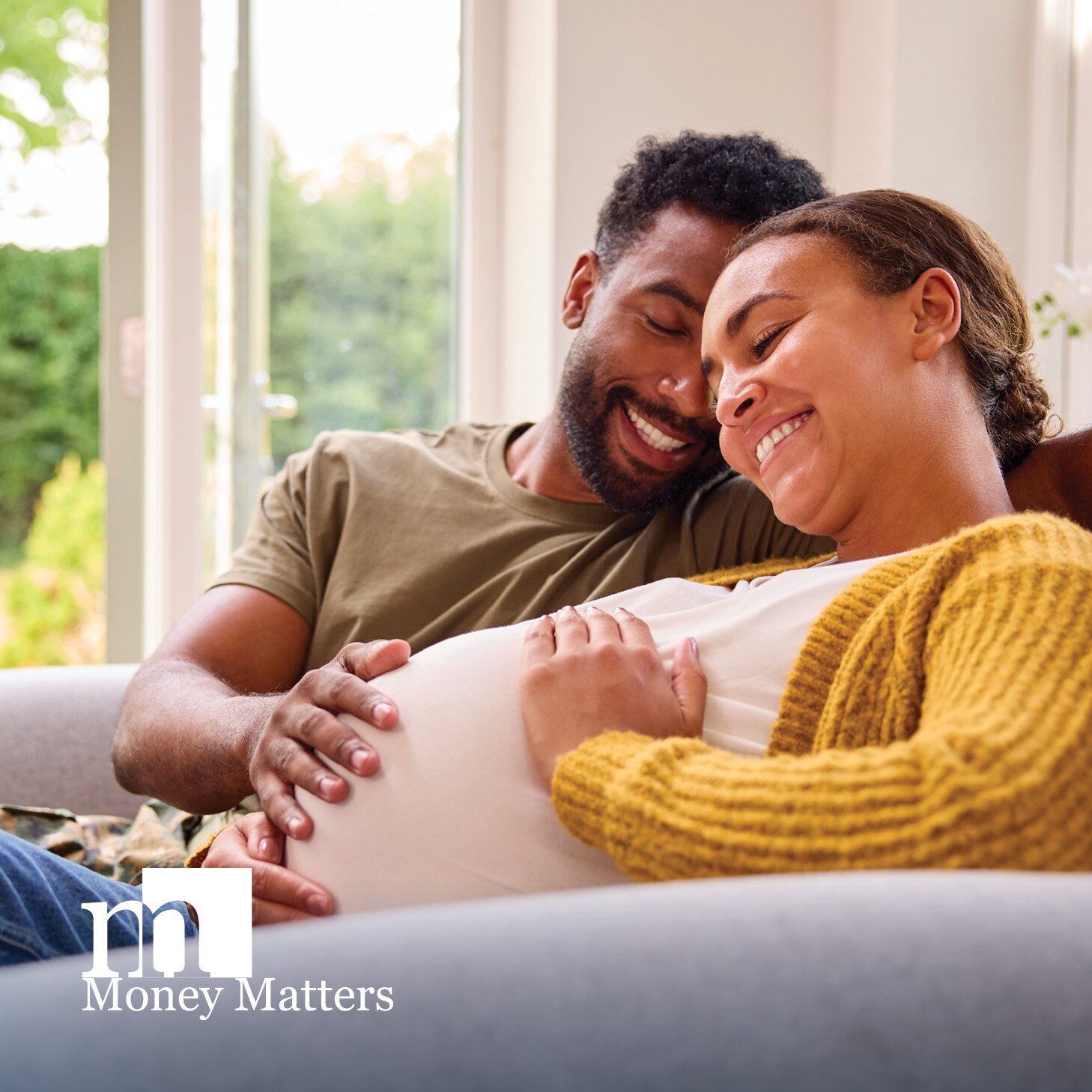 A man and a pregnant woman sit on a couch, smiling.