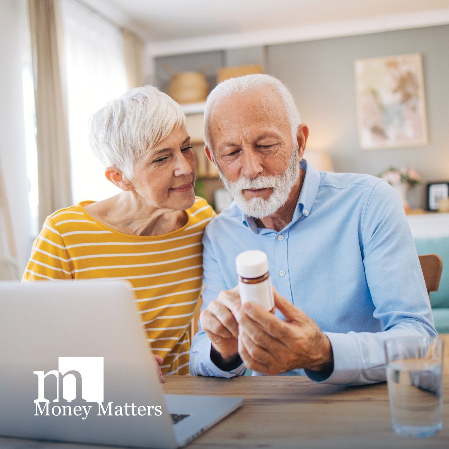 A man and woman sit in front of a laptop, looking at a prescription bottle.