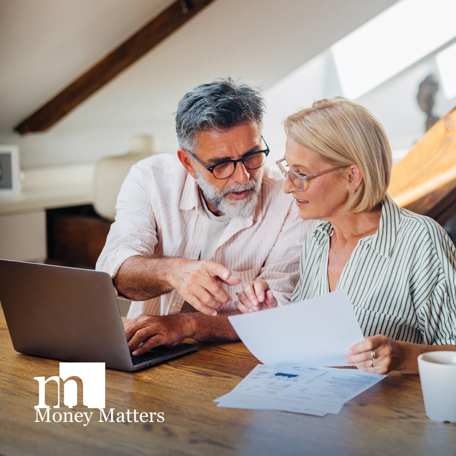 A man and a woman sit at a laptop, holding paperwork.