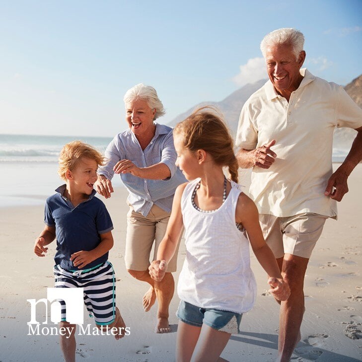 An older man and woman run on a beach with a young girl and boy.