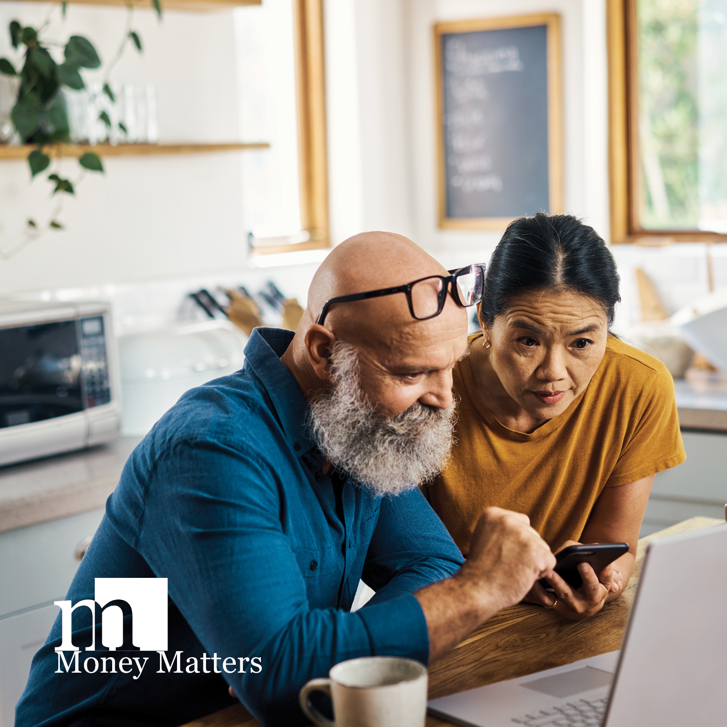 A man and a woman look at a laptop in their kitchen.