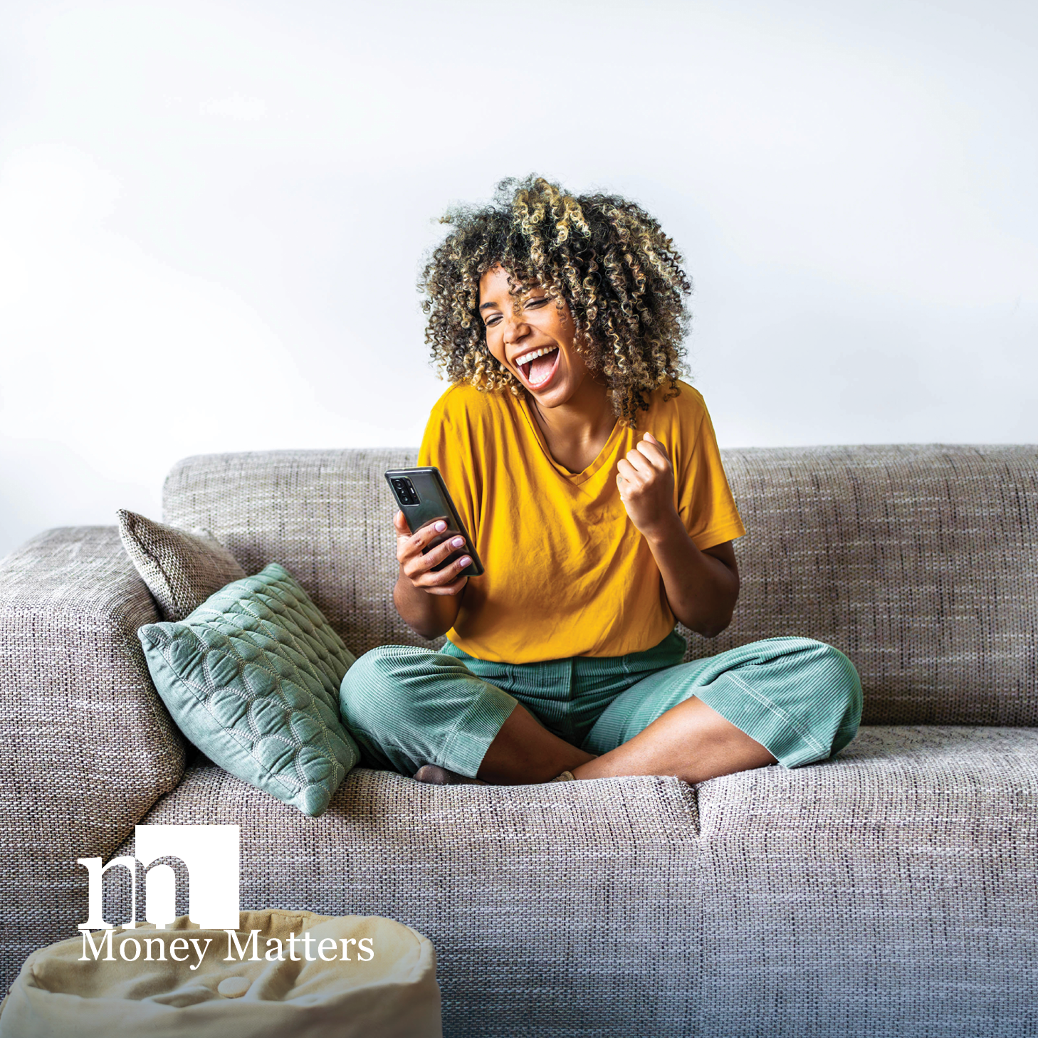 A woman sits on a couch, looking at her phone.