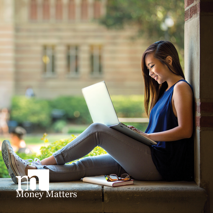 A young woman sits on a wall with a laptop.