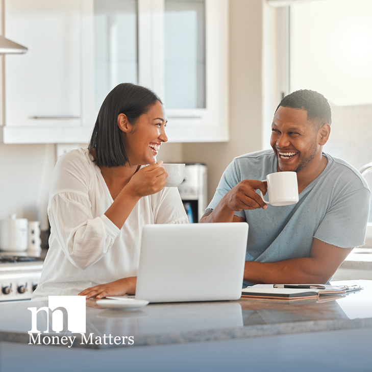 A man and woman sit at a kitchen counter, drinking coffee and looking at a laptop