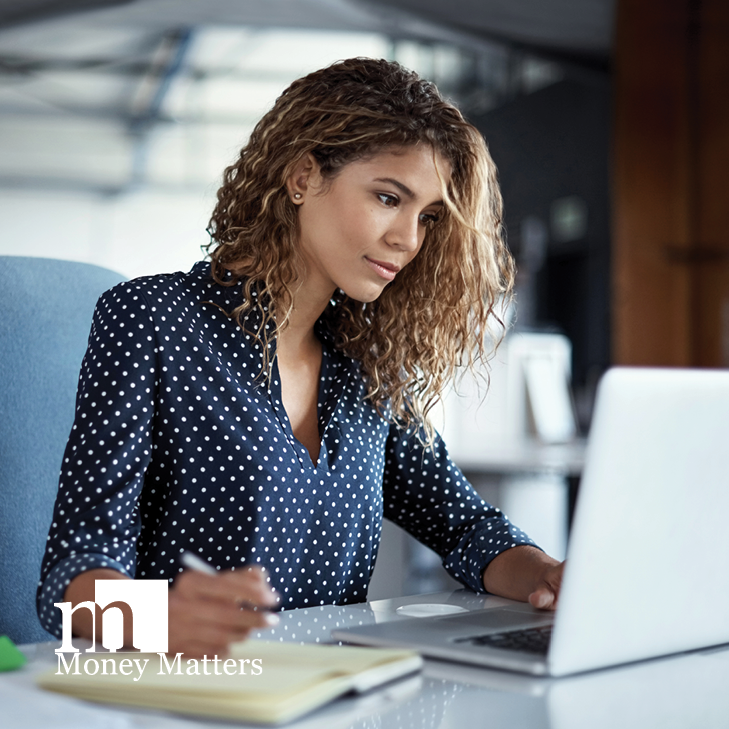 A woman sits at a desk, looking at a laptop.