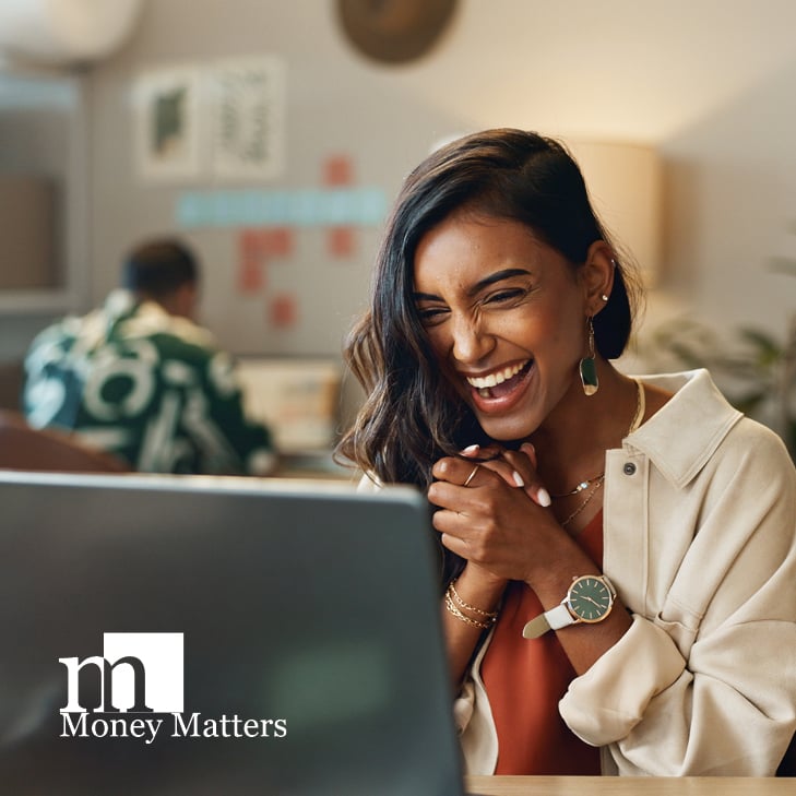 A woman sits looking at a laptop.