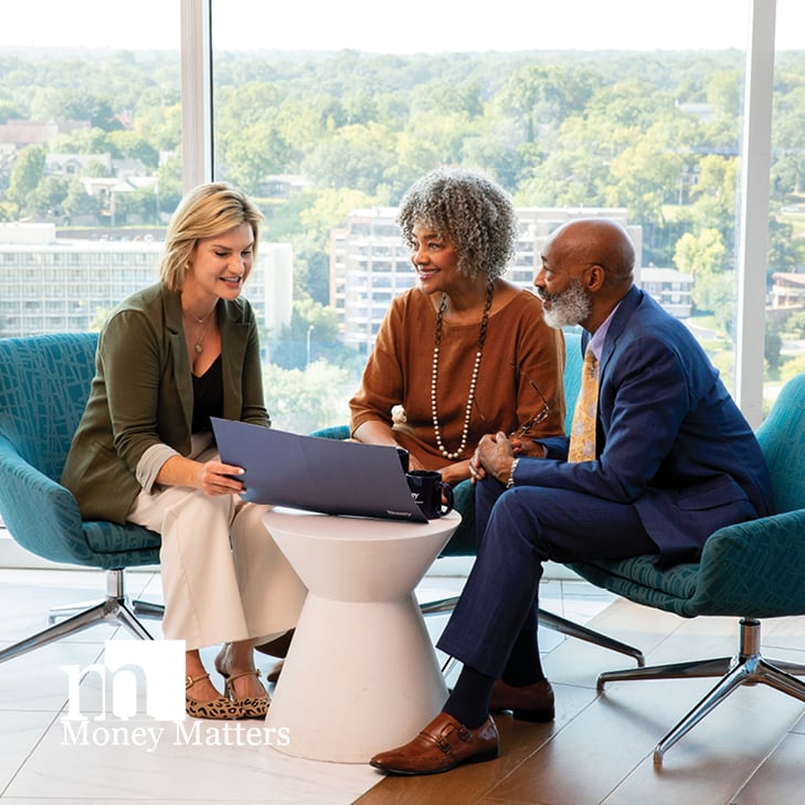 A man and woman are sitting at a table, talking to another woman who has a laptop.
