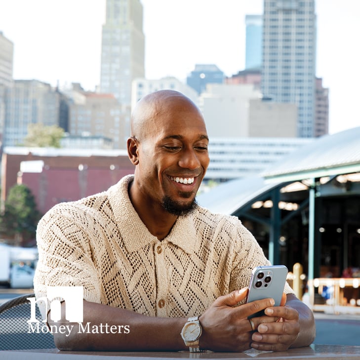 A man sits outside, looking at his cell phone.